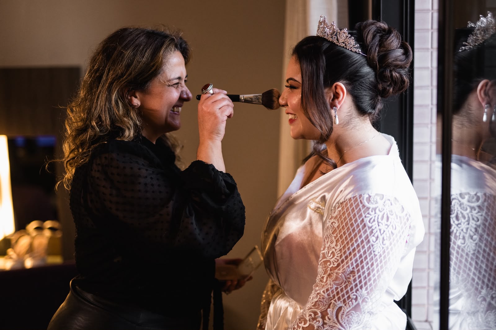 Auridiana passando maquiagem em noiva com tiara, ambas sorrindo